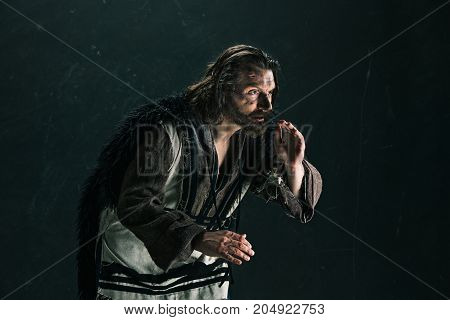 Actor in makeup, a poor man on black studio background. The bum in canvas rags. concept of vagrancy and survival