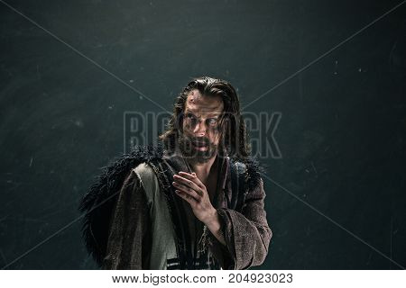 Actor in makeup, a poor man on black studio background. The bum in canvas rags. concept of vagrancy and survival