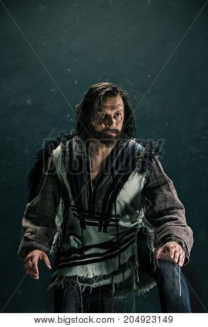 Actor in makeup, a poor man on black studio background. The bum in canvas rags. concept of vagrancy and survival