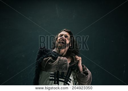 Actor in makeup, a poor man on black studio background. The bum in canvas rags. concept of vagrancy and survival