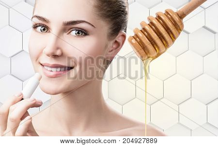 Young woman putting organic lipbalm with honey on lips over gray honeycombs background.