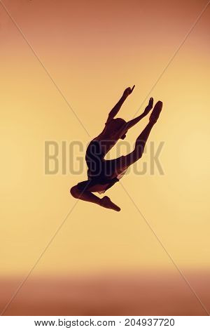 Beautiful young ballet dancer jumping on orange background.