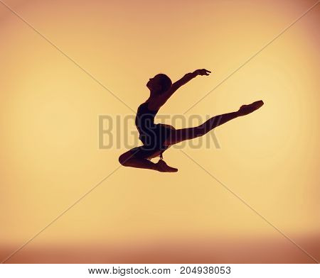 Beautiful young ballet dancer jumping on orange background.