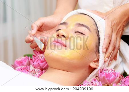 Happy Relax Woman Getting Gold Facial Mask At Beauty Salon.