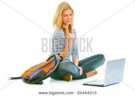 Lieto teengirl seduto sul pavimento con zainetto e laptop isolata on white