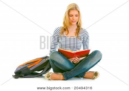 Teengirl pensoso con zainetto seduto sul pavimento e leggendo il libro isolata on white