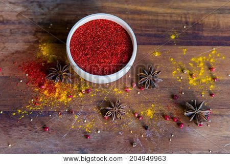 Close up white wooden bowl filled with paprika powder on dark wooden surface covered with anise and turmeric