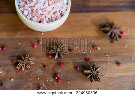 Pink Himalayan salt in a white bowl on wooden surface covered with anise and red peppercorn