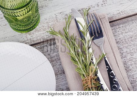 Rustic table setting with rosemary on light wooden table. Holidays decoration on Provence style. Romantic dinner.