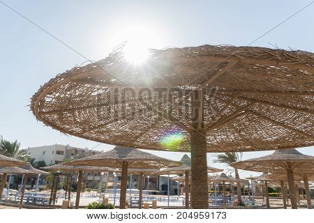 View of the sun from under the umbrella. Wicker beach umbrellas in the background.