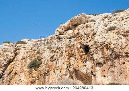 Close-up of stone rock with blue sky above with two pigeons