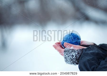 Christmas tree toy in the hands of a child. Round blue Christmas ball on snow background.