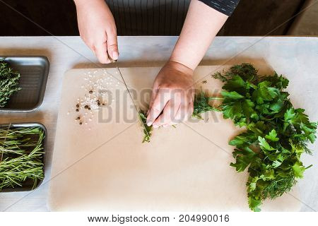 Cook chopping potherbs on wooden desk. Cooking process, healthy organic food and decoration, top view picture