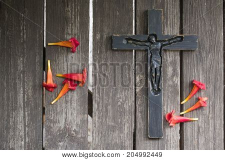 Black Wooden Crucifix On The Shabby Wooden  Plank With Red Flowers.
