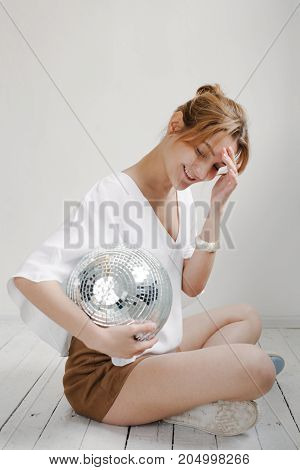 Young Hipster Woman Holding Disco Ball And Posing Cheerfully On White Background