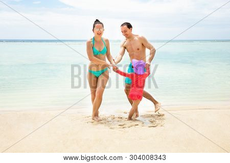 Happy Parents Enjoying Playing With Little Daughter Near The Coast At Idyllic Beach