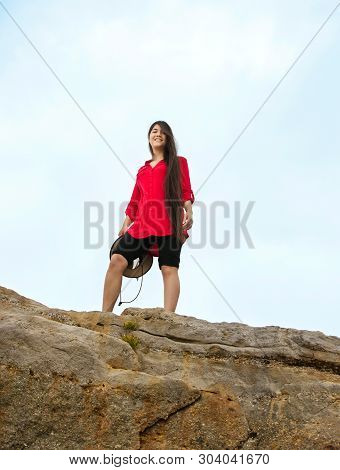 Biracial Caucasian  Asian Teen Girl With Long Hair In Red Shirt Standing On Top Of High Rocky Summit