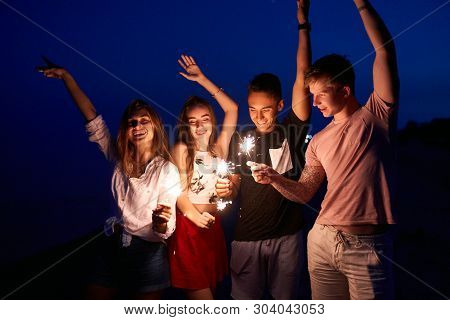 Friends Walking, Dancing And Having Fun During Night Party At The Seaside With Bengal Sparkler Light