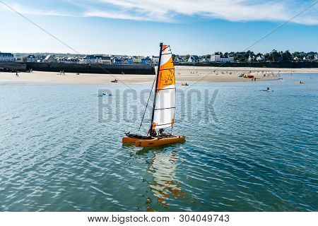 Morgat, France - August 4, 2018:  Catamaran Sailing In The Port Of Morgat Against The Beach And The 