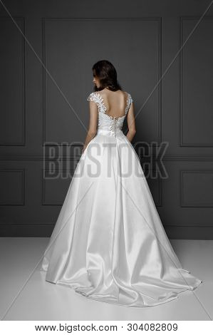 Back View Of A Tender Brunette Model In White Delicate Princess Wedding Dress, Isolated On A Grey Ba