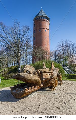 Grimmen, Germany - April 17, 2019: Wooden Dragon Sculpture In Front Of The Water Tower In Grimmen, G