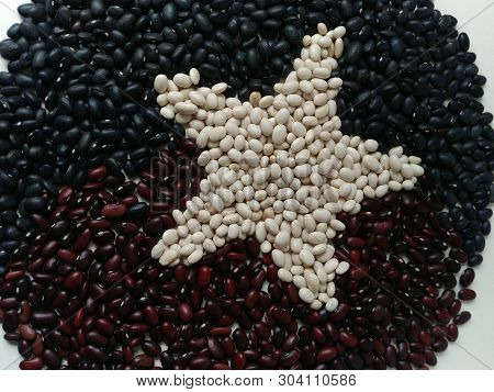 Star Of White Beans In A Circle Of Black And Red Beans. Top View. Flat Layout. The Surface On A Whit