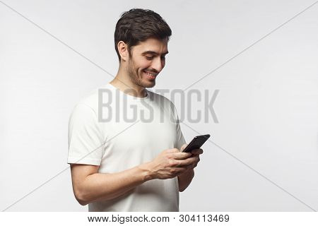 Side Portrait Of Handsome Man, Isolated On Gray Background, Looking Down At Smartphone Screen, Excha