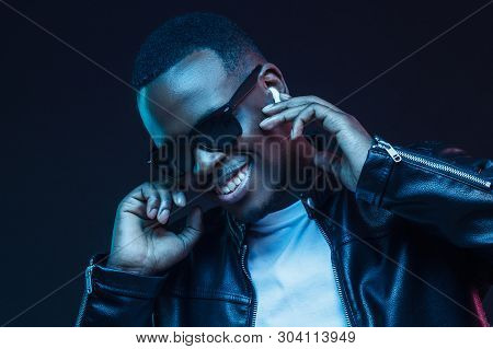 Smiling African Male Listening To Music Via Wireless Earphones At Night