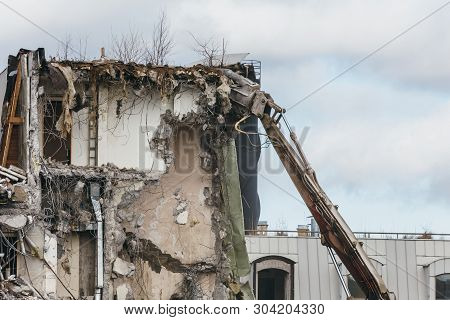 Excavator With Long Mechanical Arm At Height Breaks Off Pieces Of The House. Cleaning Area For A New