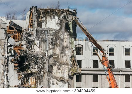 Excavator With Long Mechanical Arm At Height Breaks Off Pieces Of The House. Cleaning Area For A New