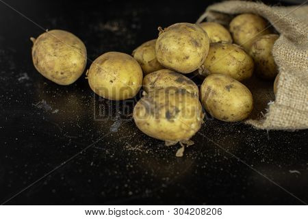 Potatoes On Black Surfase In A Canvas Bag. Fresh Potato With Traces Of Earth On The Skin. Dirty Raw 