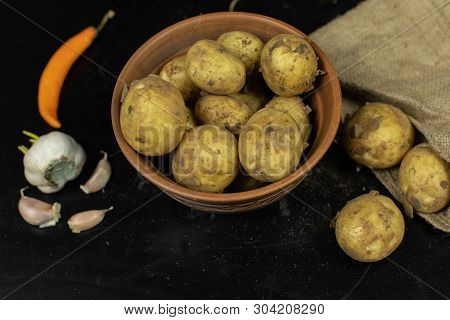 Potatoes On Black Surfase On A Plate. Fresh Potato With Traces Of Earth On The Skin. Dirty Raw Potat