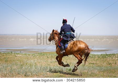 Don Cossack In Blue Military Clothes Quickly Rides Along The Coast Of The Sea With A Sabre In His Ha