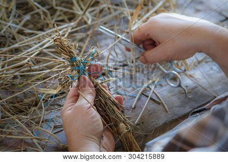 Straw Toy In The Form Of A Cross In The Hands Of An Elderly Woman