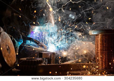 Welder is welding metal part in industrial workshop.