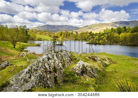 The Picturesque Tarn Hows Showing The Water And The Rocky Shore Side. Part Of The National Park At C