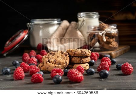 Raspberries, Blueberries And Cookies In Focus, Milk And Flour Sealed Jars In Background