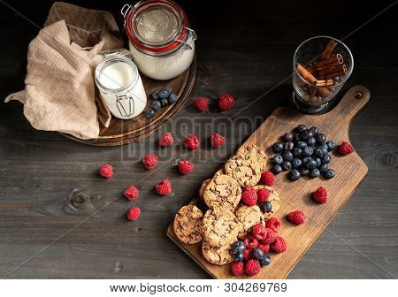 Table Top Stacked Chocolate Cookies And Berries Next To Milk And Cinnamon Sticks