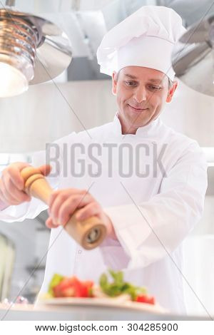 Confident mature chef using peppermill on salad in plate at restaurant