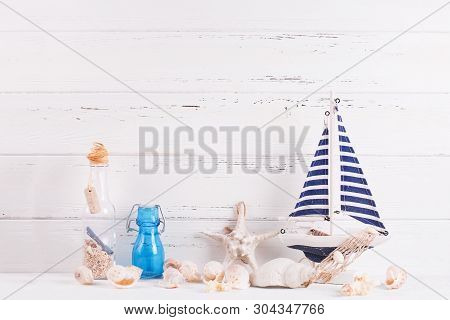 Marine Decorations Near By Wooden White  Wall. Decorative Boat Or Ship, Star Fish, Shells, Blue Bott
