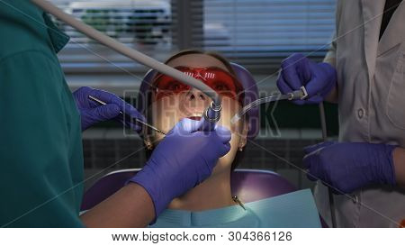 Dentist Is Taking Care About Patients Tooth Using Electric Dental Brush. Nurse With Saliva Ejector N