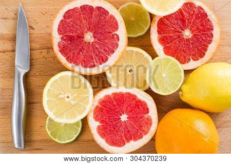 Sliced Fresh Citrus (lemons, Limes, Grapefruits, Oranges) On A Wooden Cutting Board With A Metal Kni