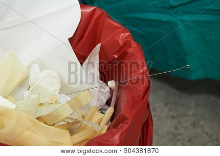 Close-up View Of Gloves, Paper And Surgical Stylet In Red Garbage Bin