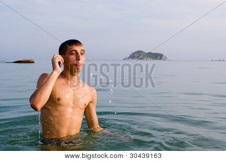 der junge Mann kommt aus dem Wasser. hat Wasser aus dem Mund spuckte und spricht von Mobile.