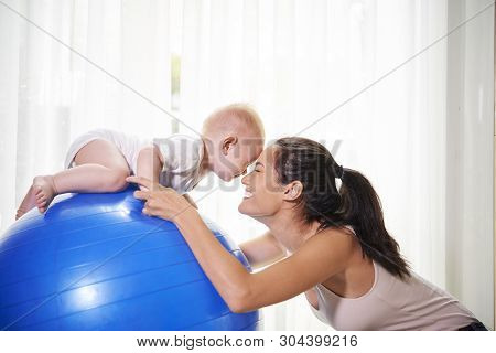 Happy Slim Young Mother Exrcising On Fitness Ball With Her Baby Boy At Home