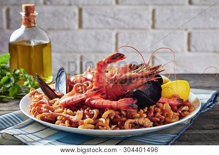 Spanish Fideua, A Noodle Paella With Prawns, Fish, Calamari, Mussels Served On A White Plate On A Gr