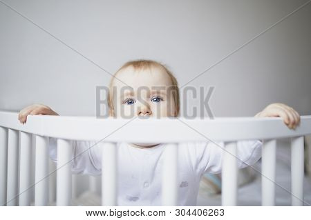 Adorable Baby Girl In Co-sleeper Crib Attached To Parents Bed. Little Kid Sitting In Cot