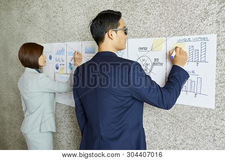 Vietnamese Business People Taking Notes On Charts And Digrams Hanging On Wall In Office