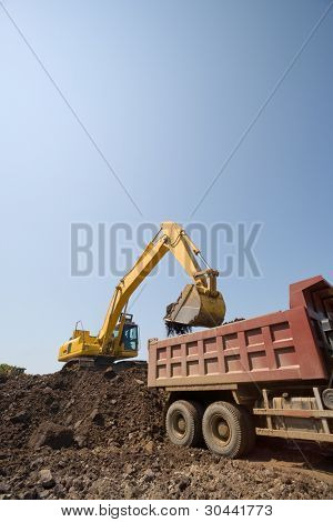 Der Bagger lädt einem LKW einen irdenen Boden