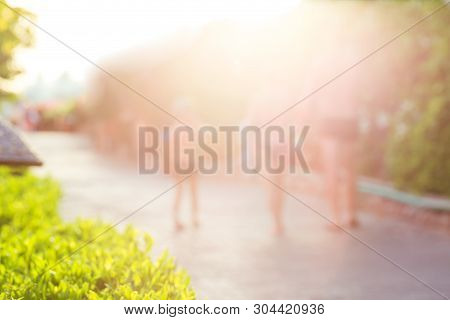 Blurred Family Disappearing In Summer Evening Glow With Sunlit Bush Geenery In Front. Summer Vacatio
